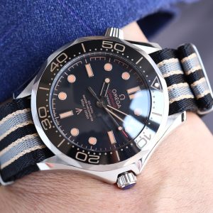 The Seamaster 007 Edition features a 42mm titanium case with a black aluminum diving bezel adorned with brown markings, offering exceptional water resistance. Its black dial, also crafted from aluminum alloy, incorporates brown markings and bears the British Royal Property "Broad Arrow" triangular arrowhead emblem at the 6 o'clock position.Powered by the Master-certified bidirectional automatic 8806 movement, this 007 edition features a solid caseback engraved with the 007 emblem and a series of codes: "0552" signifies naval service, "9237697" denotes a diver's watch, and the letter "A" indicates a screw-down crown.The final "62" signifies the year 1962 when the film Dr. No was released. The watch comes with a titanium Milanese mesh bracelet with folding clasp and a NATO strap. The box is made of canvas and houses an imported ETA mechanical movement. Royal continues to deliver premium quality.